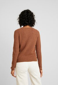 Brauner gerippter Pullover mit langen Ärmeln, tailliertem Design und rundem Halsausschnitt, getragen über cremefarbenen Cordhosen.