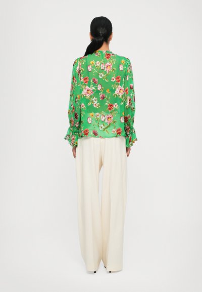 Floral green blouse with ruffled sleeves, paired with cream wide-leg pants. Features vibrant floral patterns on smooth fabric.