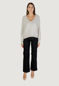Pull en maille gris clair avec un col en V, des manches longues et une coupe décontractée, associé à un jean noir évasé et des escarpins nude.