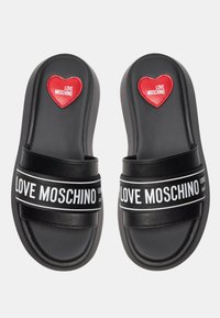 Sandali platform neri con fasce larghe. Testo "LOVE MOSCHINO" in bianco sulla fascia. Presenta un accento a forma di cuore rosso sulla punta.