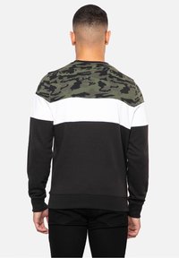 Zwart-witte en camouflagegroene sweater met ronde hals en lange mouwen, voorzien van een colorblock-ontwerp en een zachte textuur. Achteraanzicht weergegeven.