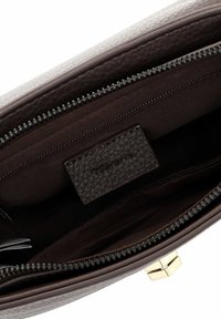 Braunes, strukturiertes Lederhandtascheninnere mit einem Reißverschluss, versehen mit einem dunklen Stofffutter und einem Markenetikett. Sichtbare Hardware-Details in Goldoptik.