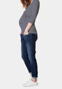 Graviditetstopp med marinblå och vita ränder, med en frontslipsdetalj, tillsammans med mörka denimjeans och vita sneakers.