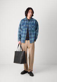 Rutete jeansjakke i blåtoner, svart skjorte, beige bukser og en svart lær totebag. Holdbare materialer med funksjonelle detaljer.