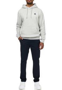 Sudadera con capucha de color gris claro, con un bolsillo delantero y un logo, combinada con pantalones azul oscuro y zapatillas blancas. Corte estándar y material de algodón.