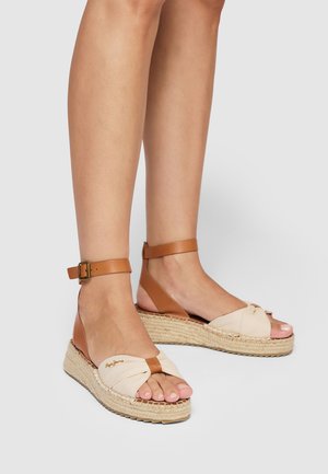 Sandalias de cuña de tela beige con correas marrones en el tobillo, suela de yute trenzado, detalle de nudo en la zona del dedo y sutil adorno de logo.