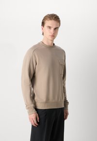 Sweatshirt beige a girocollo realizzato in morbido tessuto, con tasca frontale, polsini e orlo a coste, dal taglio rilassato e dalla texture liscia.