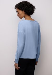 Světle modrý dlouhý rukáv s uvolněným střihem, zdobený texturovanými akcenty podél rukávů a širokým výstřihem. Hladká látka.