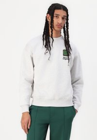 Heledhalli särk pehmest materjalist, millel on mugav lõige, soonikkoes mansetid ja rinnal väike roheline embleem.