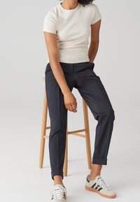 Vit ribbad kortärmad topp, marinblå skräddarsydda byxor med sidofickor, uppvikta ärmslut och ljusa sneakers med svarta accenter.