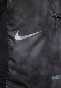 Tissu noir avec un logo Nike swoosh argenté et une fermeture éclair sur le côté droit du panneau en tissu.