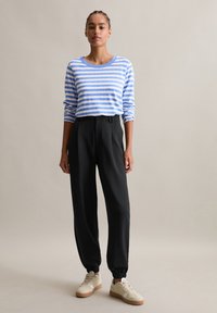 Niebiesko-biała, w paski, bluzka z długim rękawem w połączeniu z czarnymi, zwężanymi spodniami. Kremowe trampki z teksturową podeszwą. Prosty i jednolity design.