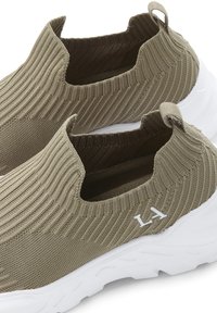 Strick-Slipper in olivgrün mit Rippstruktur, ausgestattet mit einer weißen Sohle und Logo-Akzent. Keine Schnürsenkel, elastischer Kragen für ein einfaches Anziehen.