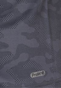 Gros plan sur un tissu gris foncé avec un motif camouflage pixelisé et une petite étiquette "ProW-B".