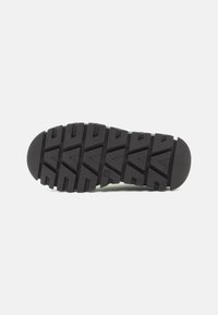 Semelle de chaussure en caoutchouc noir avec un motif de bande de roulement robuste présentant des rainures angulaires et des bords arrondis, conçue pour l'adhérence et la durabilité.