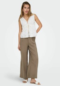 Haut sans manches blanc avec un motif à œillets, taille cintrée, associé à un pantalon en lin beige clair ample et des sandales blanches à enfiler.