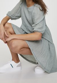 Vestido de color azul claro, texturizado, con mangas 3/4 y un corte holgado, combinado con zapatillas blancas con acentos en gris y azul.