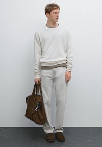 Weißer Baumwollpullover, graues Unterhemd, beige Hose, braune Wildledertasche und dunkle Schuhe. Der Look ist lässig mit strukturierten Schichten.