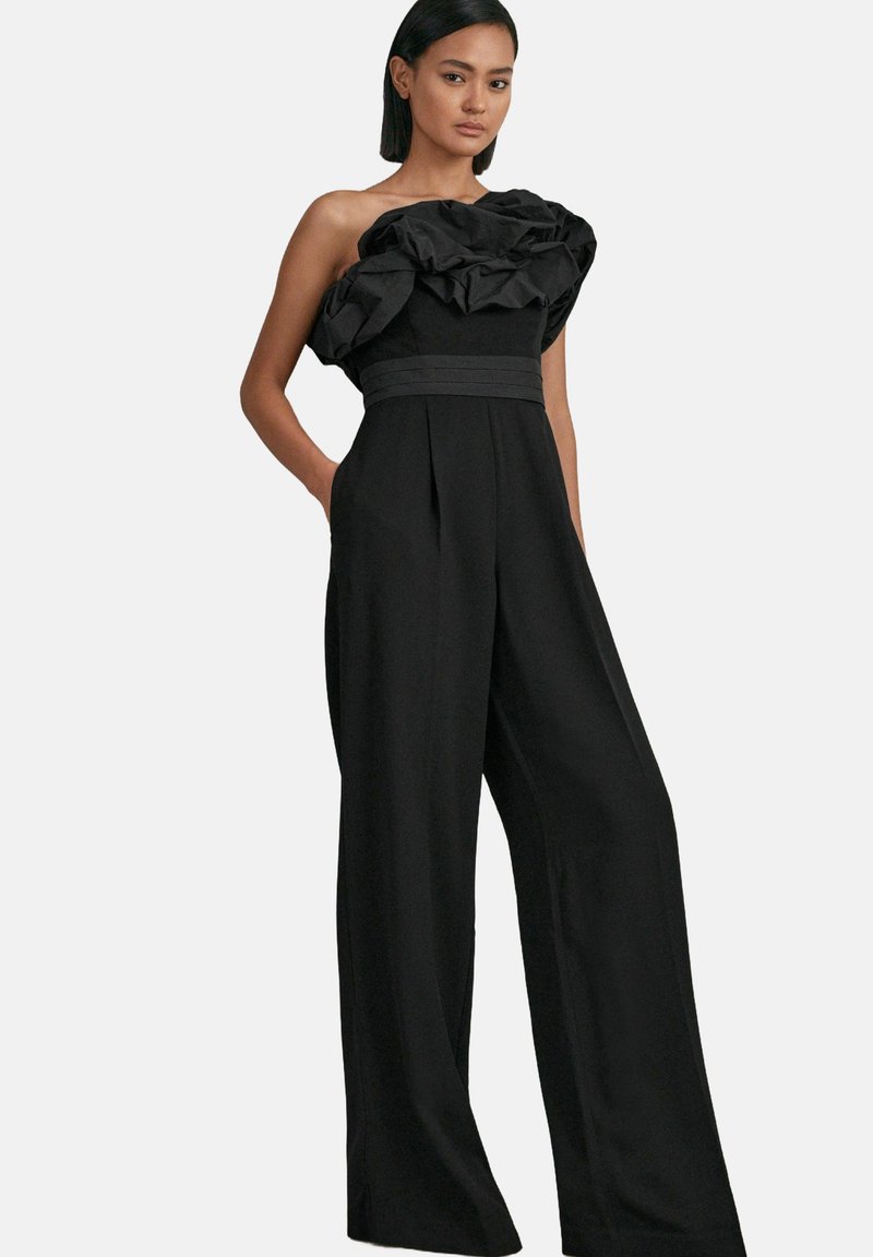 Crni kombinezon s volanima bez naramenica, širokim nogavicama i strukom koji se oblikuje. Glatka tkanina s blagim sjajem.