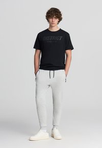Czarna koszulka z grafiką "DISTRICT", w połączeniu z jasnoszarymi zwężanymi spodniami dresowymi i białymi trampkami. Strój charakteryzuje się minimalistycznym designem.