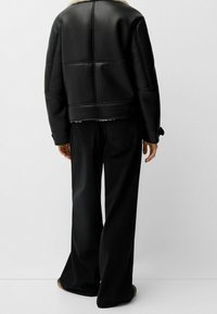 Svart läderjacka med pälskrage, med en kort silhuett och quiltad textur, tillsammans med vida svarta jeans.