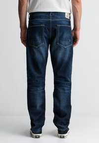 Donkerblauwe spijkerbroek met een rechte pasvorm, zichtbare stiksels, twee achterzakken en een label op de tailleband.