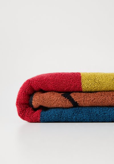 Three folded towels in red, orange, and blue with textured surfaces. The top towel features a yellow stripe and a black accent along the edge.