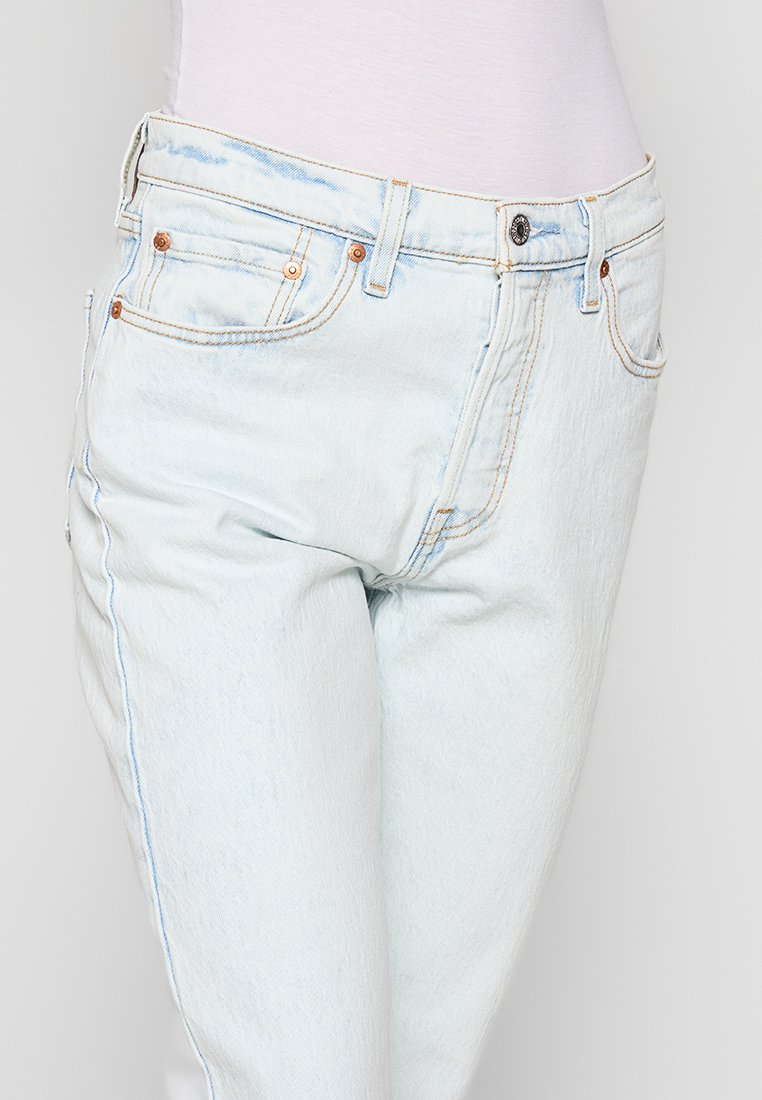 Jeans de mezclilla azul claro con cintura alta, cinco bolsillos, remaches de cobre y costuras en contraste. Textura suave con un acabado ligeramente deslavado.