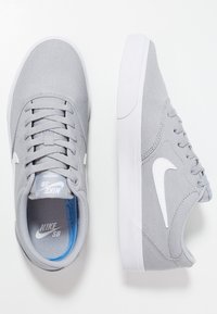 Grå canvas sneakers med vita accenter, snörning och en vit gummisula. Har en blå innersula och en framträdande swoosh-logotyp.