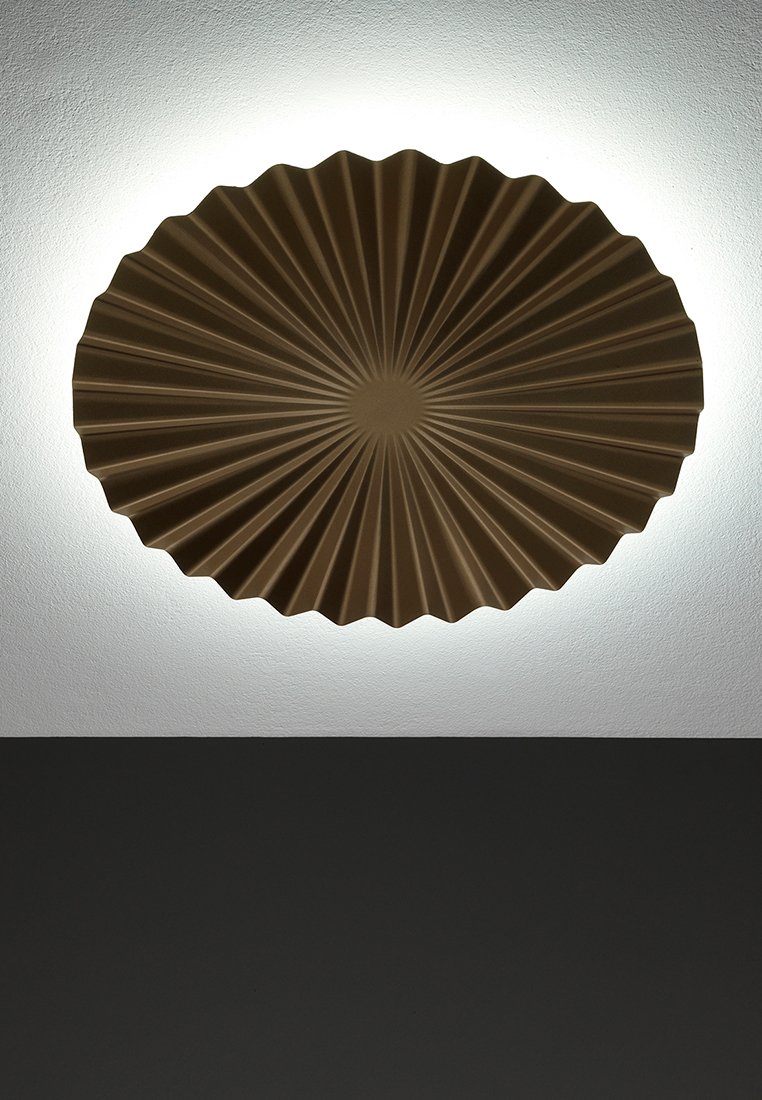 Runde, gerippte Deckenleuchte in warmem Braun mit einem Sonnenstrahl-Design, das ein sanftes Hintergrundlicht an einer weißen Wand erzeugt.