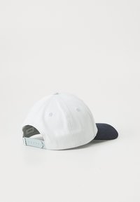 White cap with a dark blue bill, made of cotton, featuring a textured fabric and adjustable snapback closure on the back.