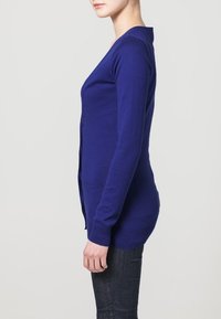 Blå långärmad kofta med en figursydd silhuett, ribbade mudd och fåll, tillverkad av mjukt material, med en enkel knappstängning framtill.