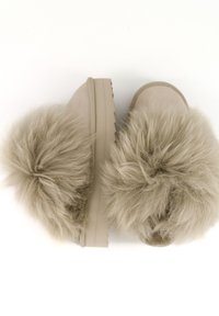 Chaussons beige à enfiler avec semelles épaisses en caoutchouc et gros pompons en fausse fourrure duveteuse sur le dessus, vus de dessus sur un fond blanc.