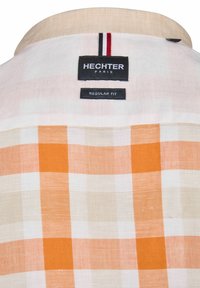 Korte mouwen, regular fit shirt in een wit, oranje en beige ruitpatroon; heeft een crèmekleurige kraag en merklabels op de achterkant.