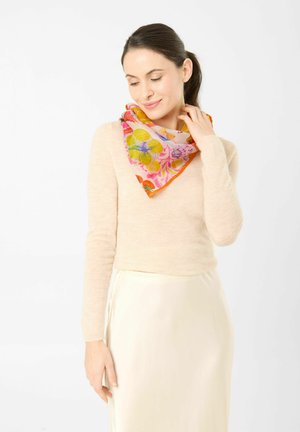 Woman wearing a beige sweater and cream skirt, touching a colorful floral scarf wrapped around her neck, looking down and smiling gently.