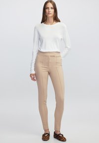 Beige fitted broek met twee voornaadse seams, gecombineerd met een witte langslavende top en leopardprint instap schoenen. Eenvoudig, strak ontwerp.