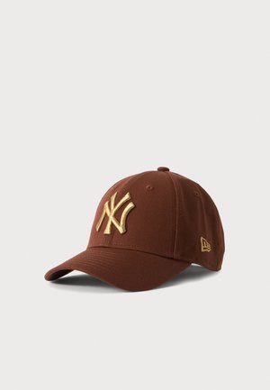 Casquette de baseball marron avec le logo doré des New York Yankees brodé sur le devant et un plus petit logo doré sur le côté.