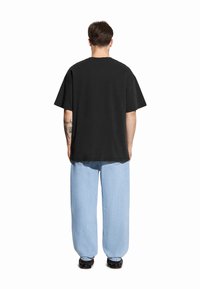 Czarna, oversize koszulka z krótkim rękawem, w połączeniu z jasnoniebieskimi, luźnymi dżinsami. Materiał bawełniany, prosty design, swobodny krój. Brak widocznych wzorów.