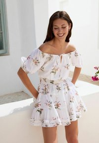 Hvid off-shoulder kjole med blomsterprint, der har en bindefront, pufærmer og en tiered, ruffles kant.
