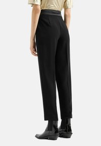 Pantaloni neri con una texture liscia, gamba affusolata e una cintura larga. Abbinati a stivaletti neri per un look elegante.