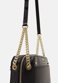 Czarna skórzana torebka o prostokątnym kształcie, wyposażona w złoty łańcuszkowy pasek, zapięcie na zamek błyskawiczny oraz metalowe ozdoby.