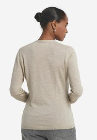 Beige långärmad stickad tröja med rund halsringning, slät textur och ribbad nederkant, sedd bakifrån.