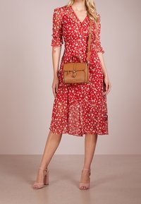 Abito floreale rosso con maniche corte, scollo a V e orlo fluido. Abbinato a una borsa a tracolla color sabbia e sandali con tacco blocco rosa.