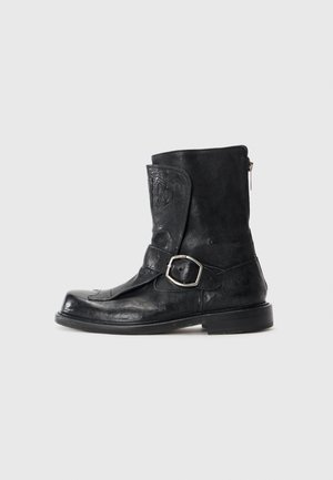 Schwarze Lederstiefel bis zur Mitte der Wade mit einem seitlichen Reißverschluss, einem dekorativen Riemen mit einer silbernen Schnalle und geprägten Details auf der vorderen Klappe.
