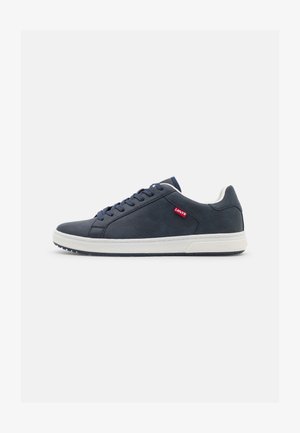 Baskets en cuir bleu marine avec semelle en caoutchouc blanc, bout rond et design à lacets. Présentent le logo rouge de Levi's sur le côté. Texture lisse.