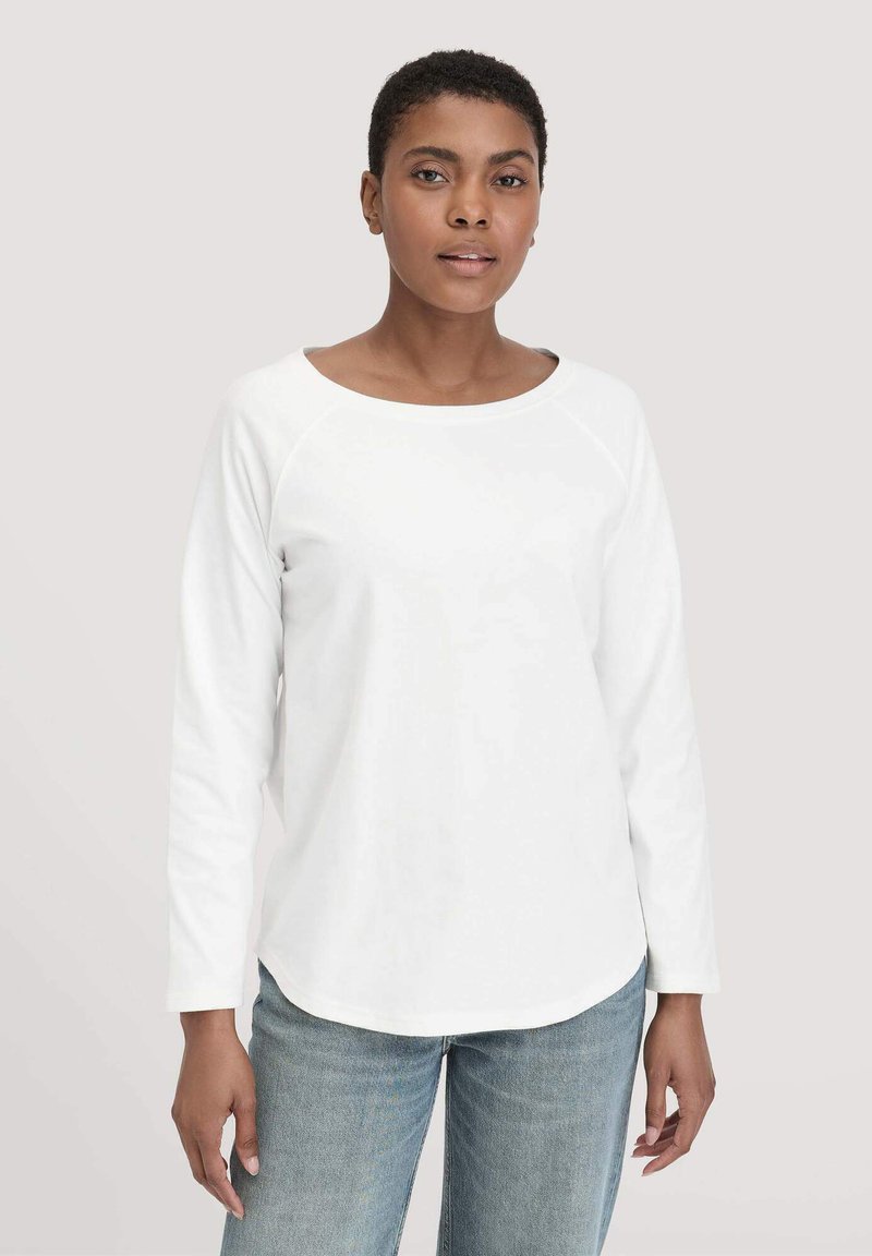 Weißes langärmliges Hemd mit rundem Halsausschnitt und Raglannähten, aus weichem Stoff. Kombiniert mit hellblauen Jeans.