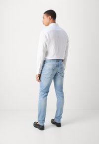 Hvit langermet skjorte med teksturert stoff, parret med lyseblå jeans med baklommer og en brun lærmerkelapp. Svarte sko.