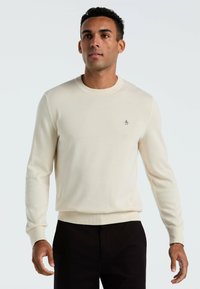 Crème kleurige sweater van zacht materiaal, met een ronde hals, lange mouwen en een klein geborduurd logo op de borst.