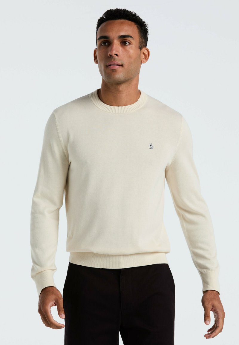 Crème kleurige sweater van zacht materiaal, met een ronde hals, lange mouwen en een klein geborduurd logo op de borst.