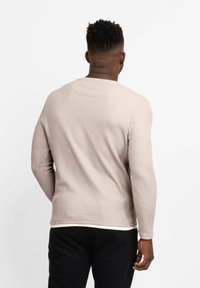 Langärmliges, geripptes Shirt in hellem Beige mit Rundhalsausschnitt und strukturiertem Stoff. Mit einem kontrastierenden Saum und enganliegenden Ärmeln gestaltet.